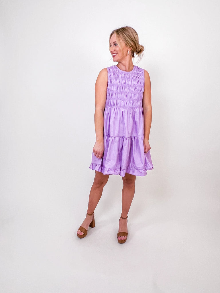Woman wearing a lavender smocked tiered mini dress with a high neckline and ruffle skirt.