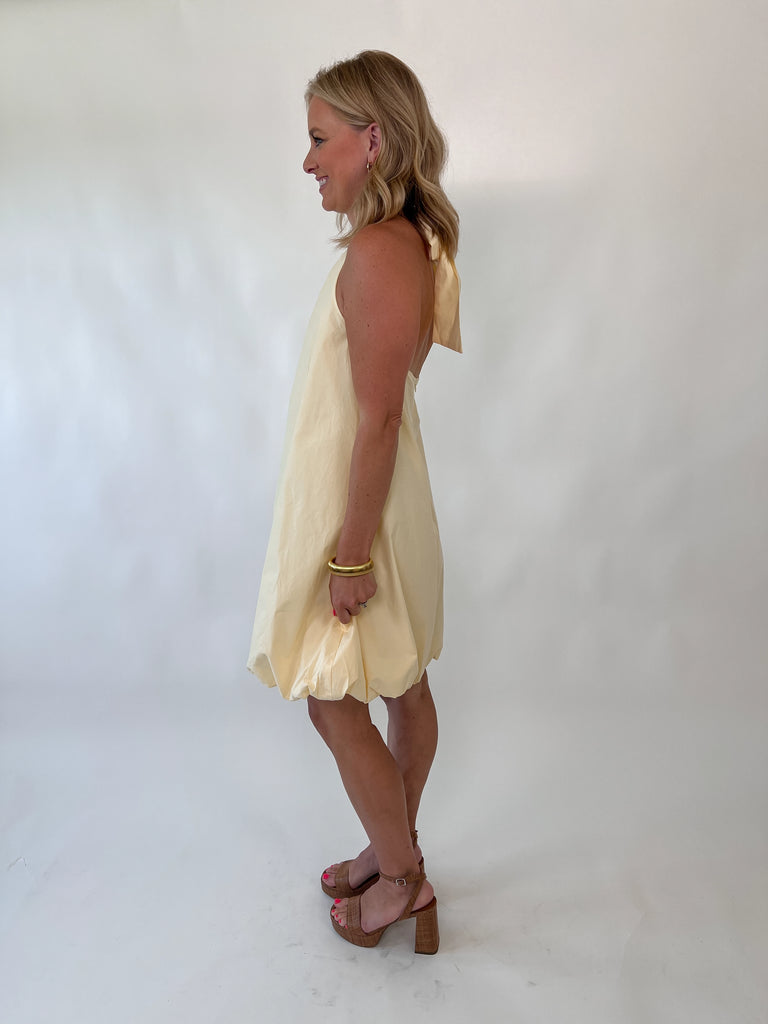 Woman wearing lemon yellow bubble hem dress with halter neckline and back bow