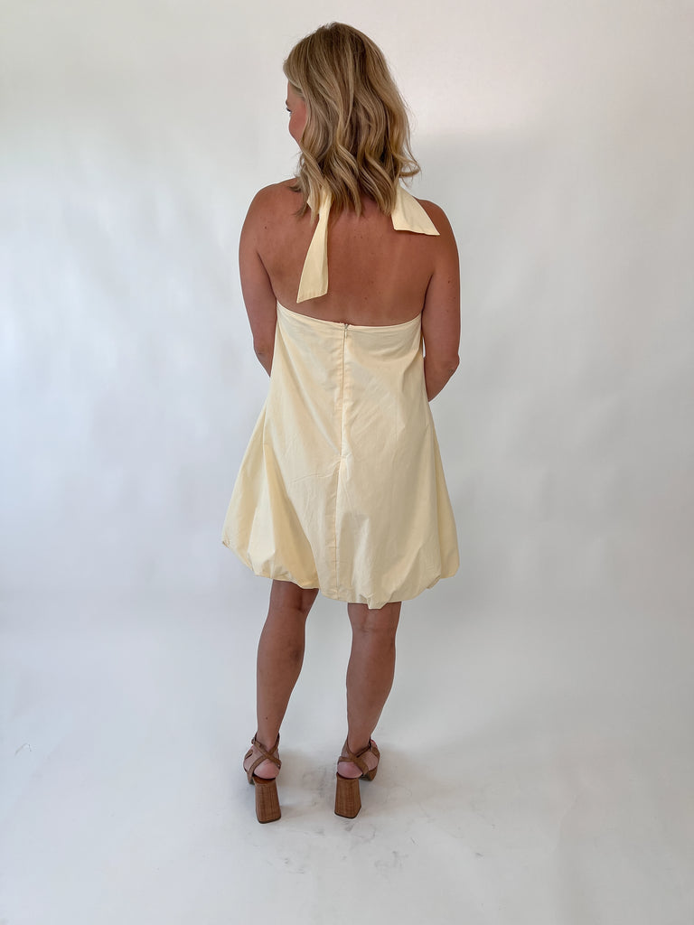 Woman wearing lemon yellow bubble hem dress with halter neckline and back bow