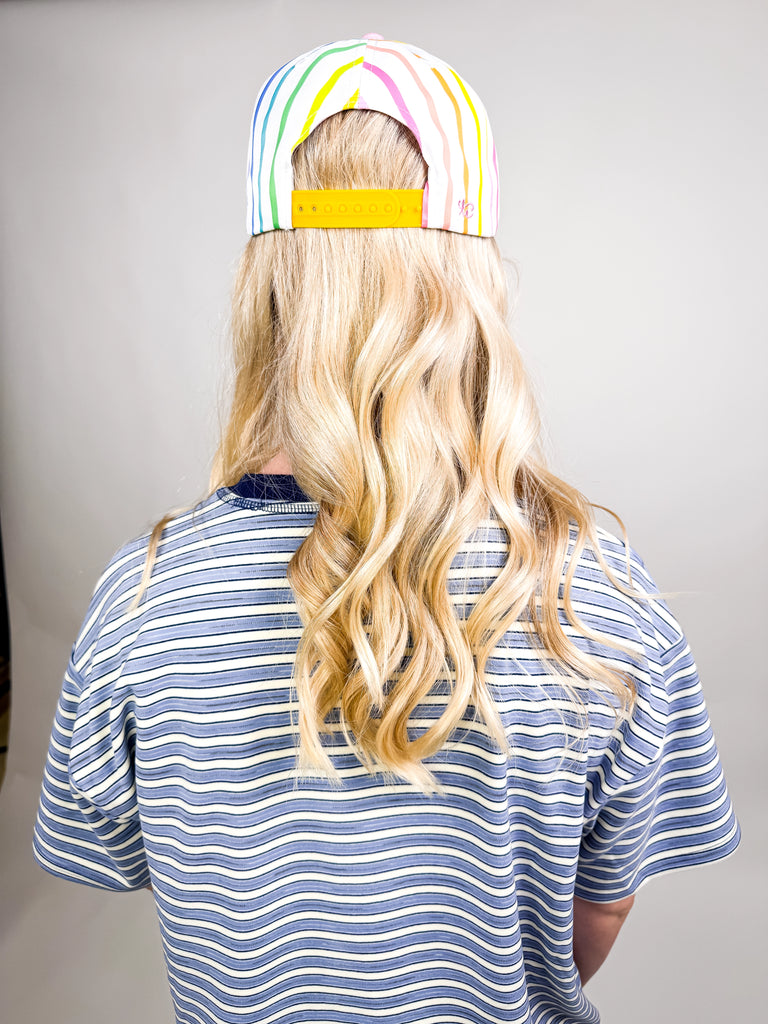 model wearing Living the Dream Baseball Cap with rainbow stripes, pink bill, and blue embroidered text