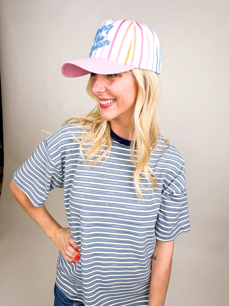 model wearing Living the Dream Baseball Cap with rainbow stripes, pink bill, and blue embroidered text