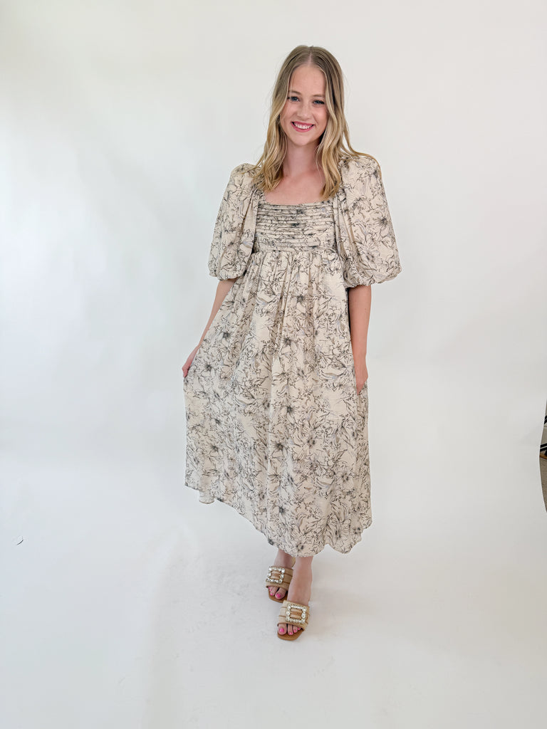 Woman wearing a neutral floral puff sleeve midi dress with an open tie-back design