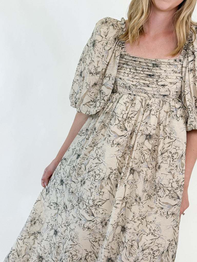 Woman wearing a neutral floral puff sleeve midi dress with an open tie-back design