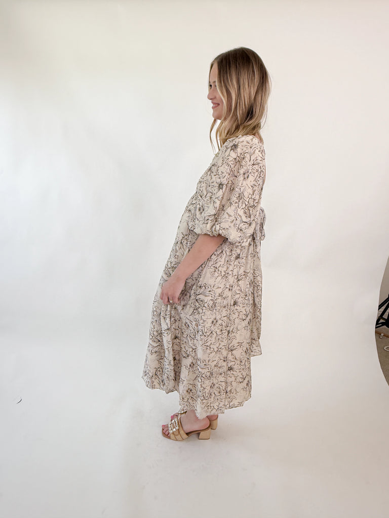 Woman wearing a neutral floral puff sleeve midi dress with an open tie-back design