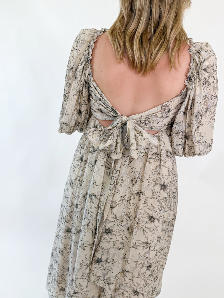 Woman wearing a neutral floral puff sleeve midi dress with an open tie-back design