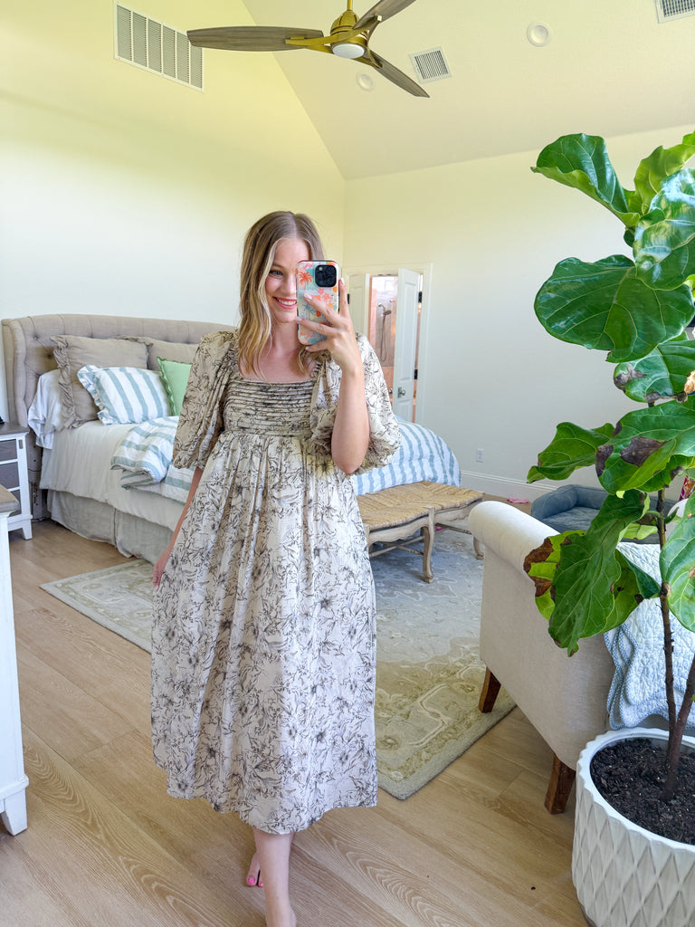 Woman wearing a neutral floral puff sleeve midi dress with an open tie-back design