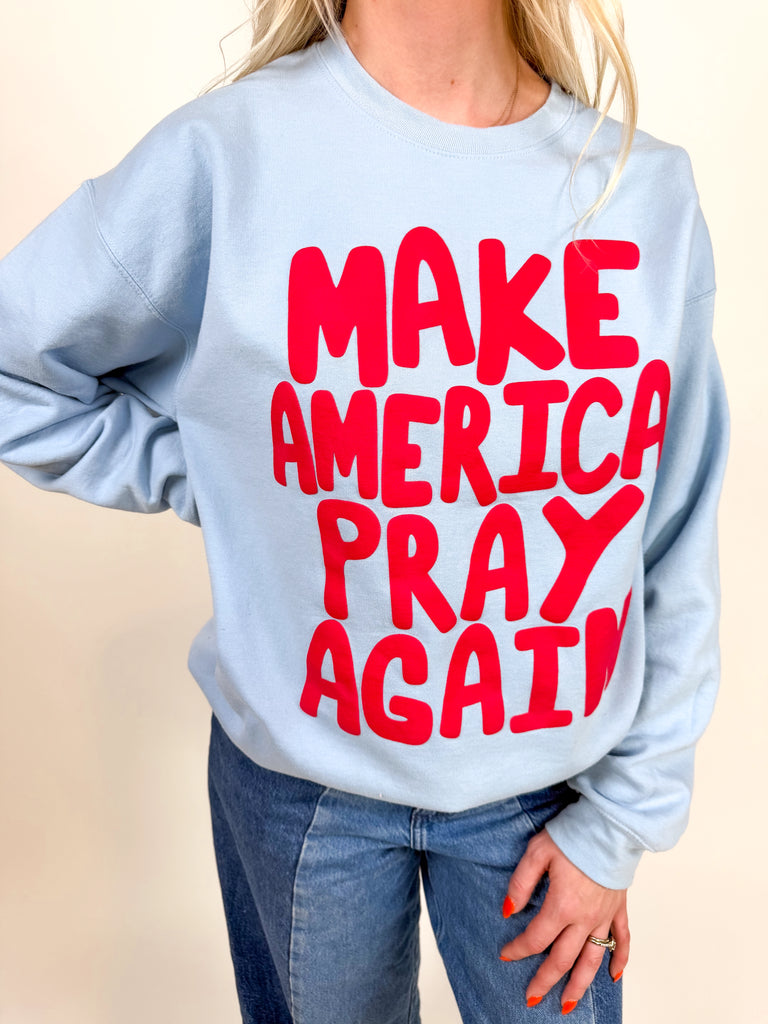 model wearing light blue sweatshirt with red “Make America Pray Again” lettering