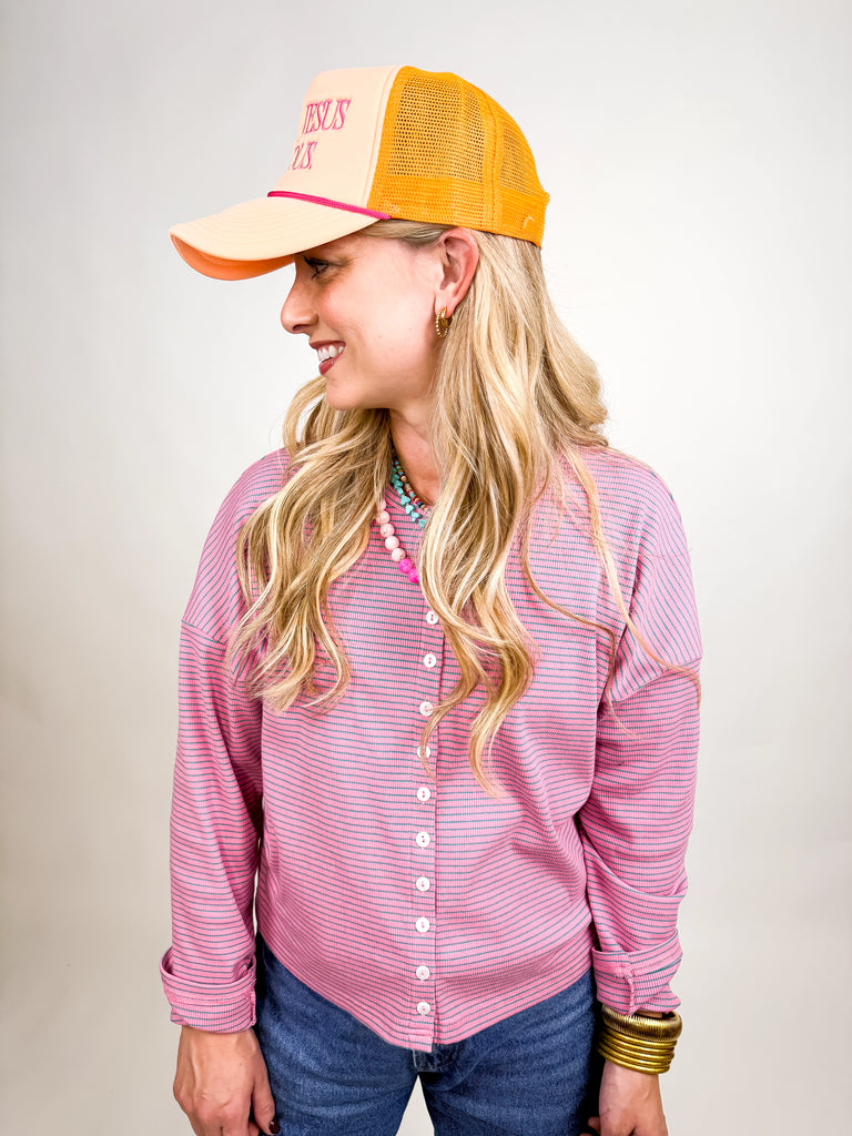model wearing Make Jesus Famous Hat with peach front, pink embroidered text, and orange mesh back