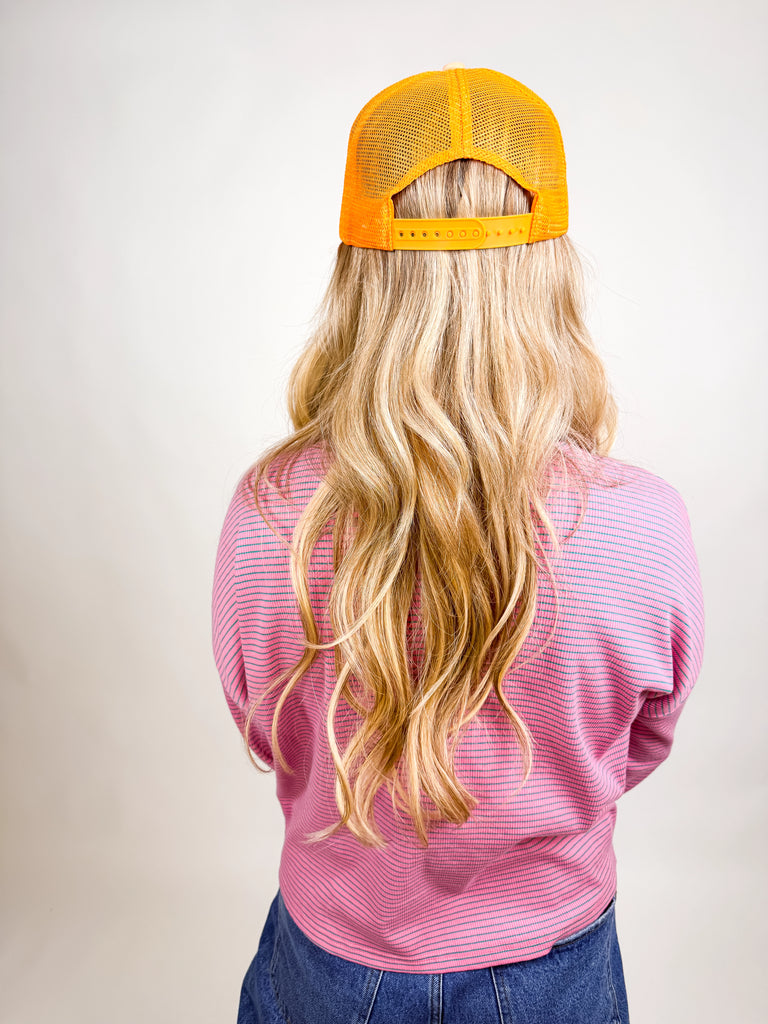 model wearing Make Jesus Famous Hat with peach front, pink embroidered text, and orange mesh back