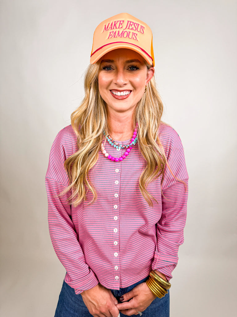 model wearing Make Jesus Famous Hat with peach front, pink embroidered text, and orange mesh back