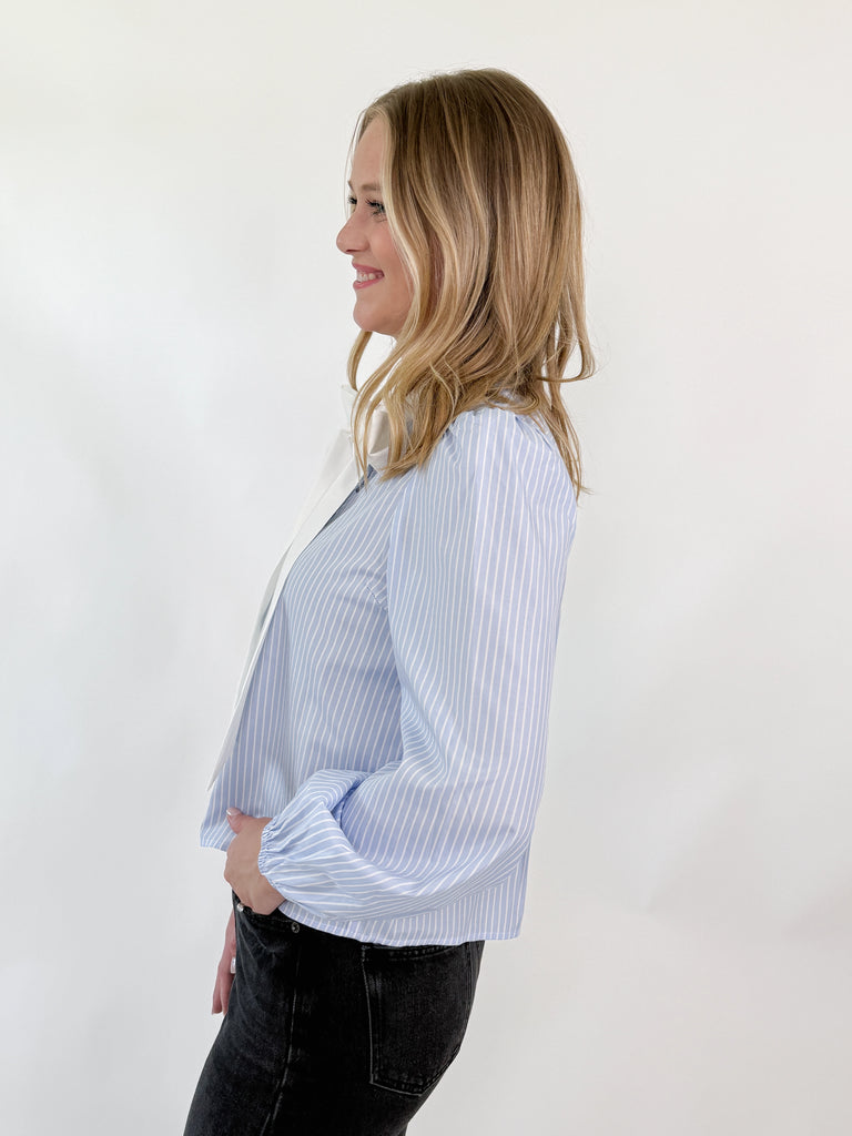 Woman wearing a blue and white pinstripe blouse with a large white bow and puff sleeves
