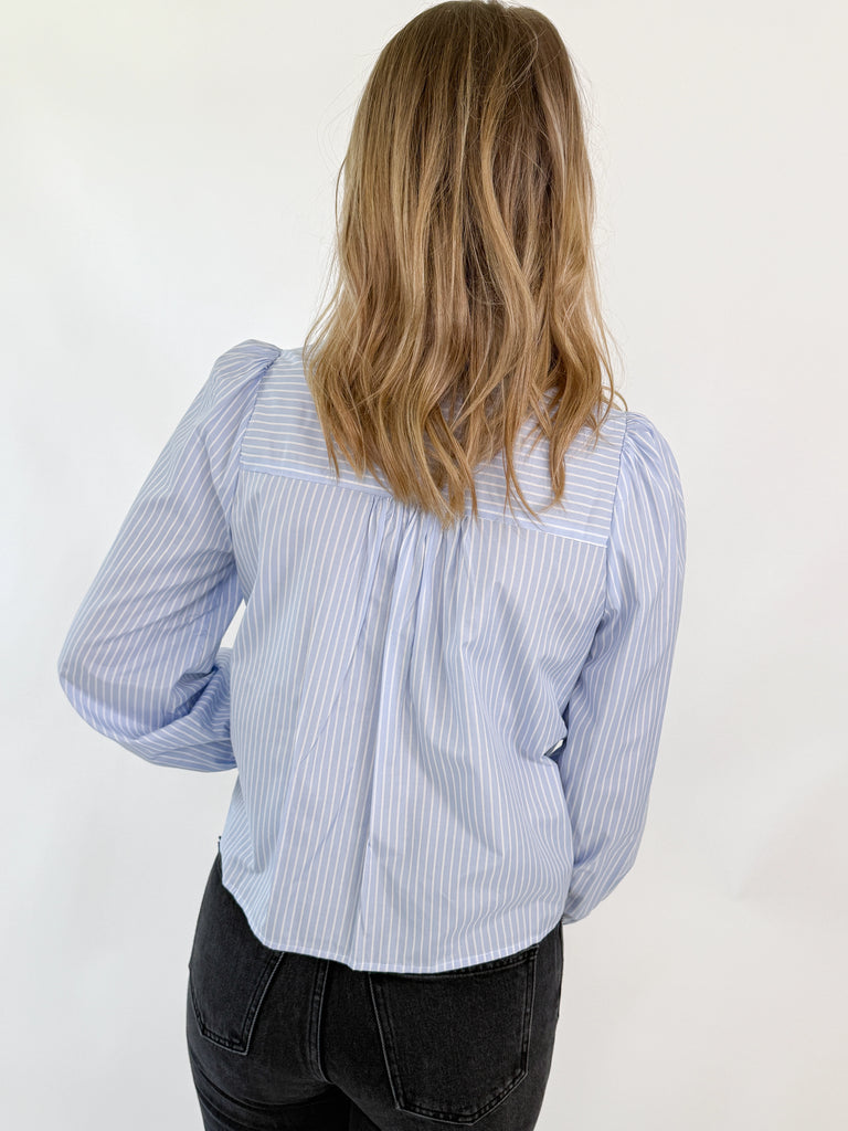 Woman wearing a blue and white pinstripe blouse with a large white bow and puff sleeves