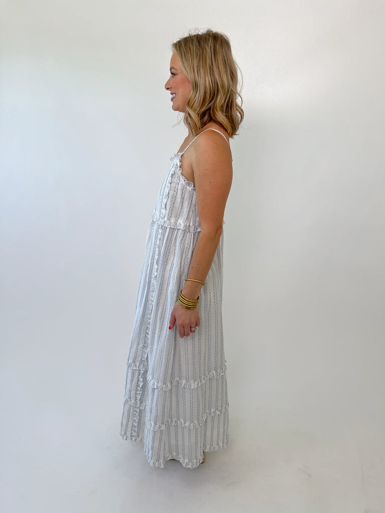 Woman wearing a blue and white striped ruffle maxi dress with adjustable straps