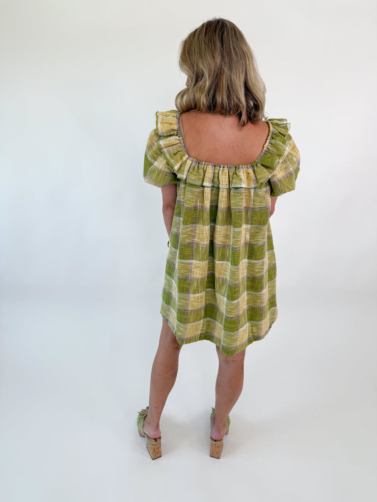Model wearing the Meadow Plaid Ruffle Mini Dress in green, yellow, and lavender plaid with ruffle neckline and short puff sleeves