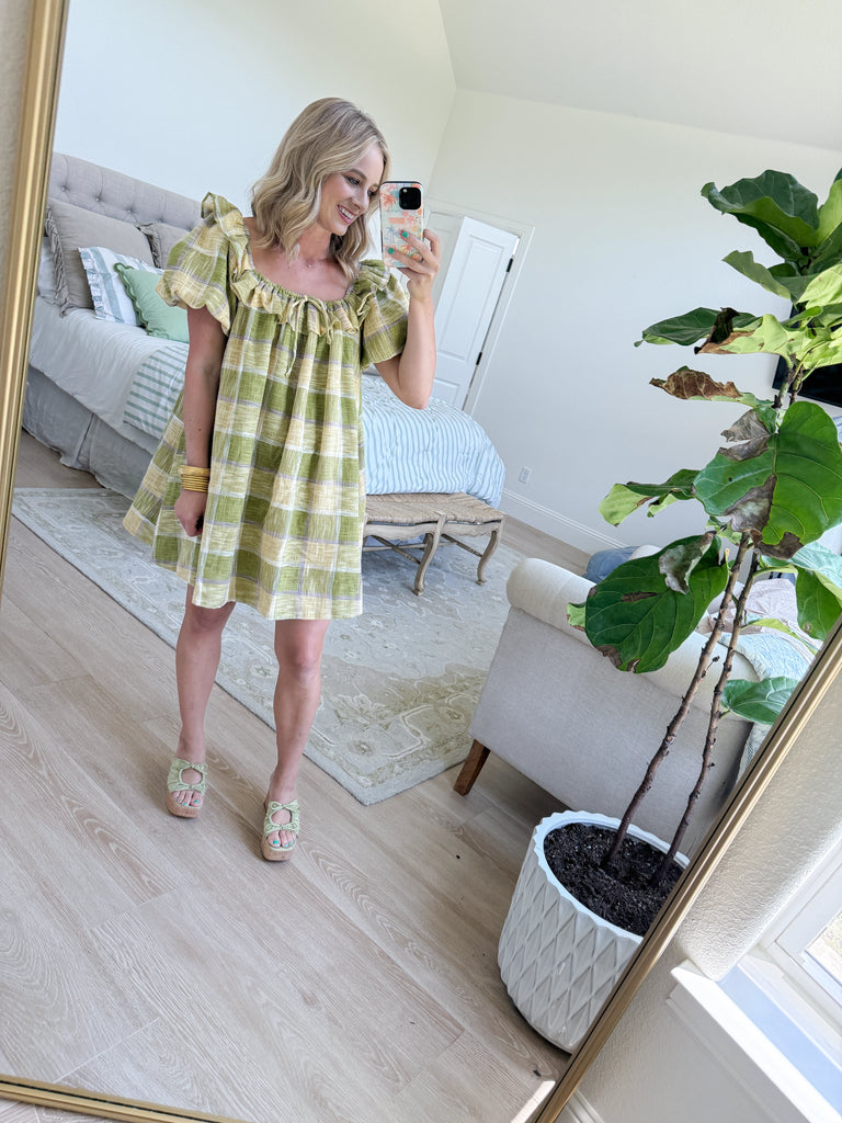 Model wearing the Meadow Plaid Ruffle Mini Dress in green, yellow, and lavender plaid with ruffle neckline and short puff sleeves