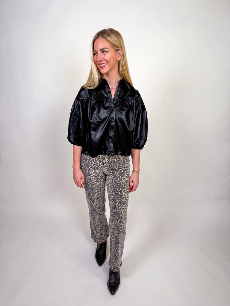 Woman wearing a black faux leather shirt with half puff sleeves and button-down front.