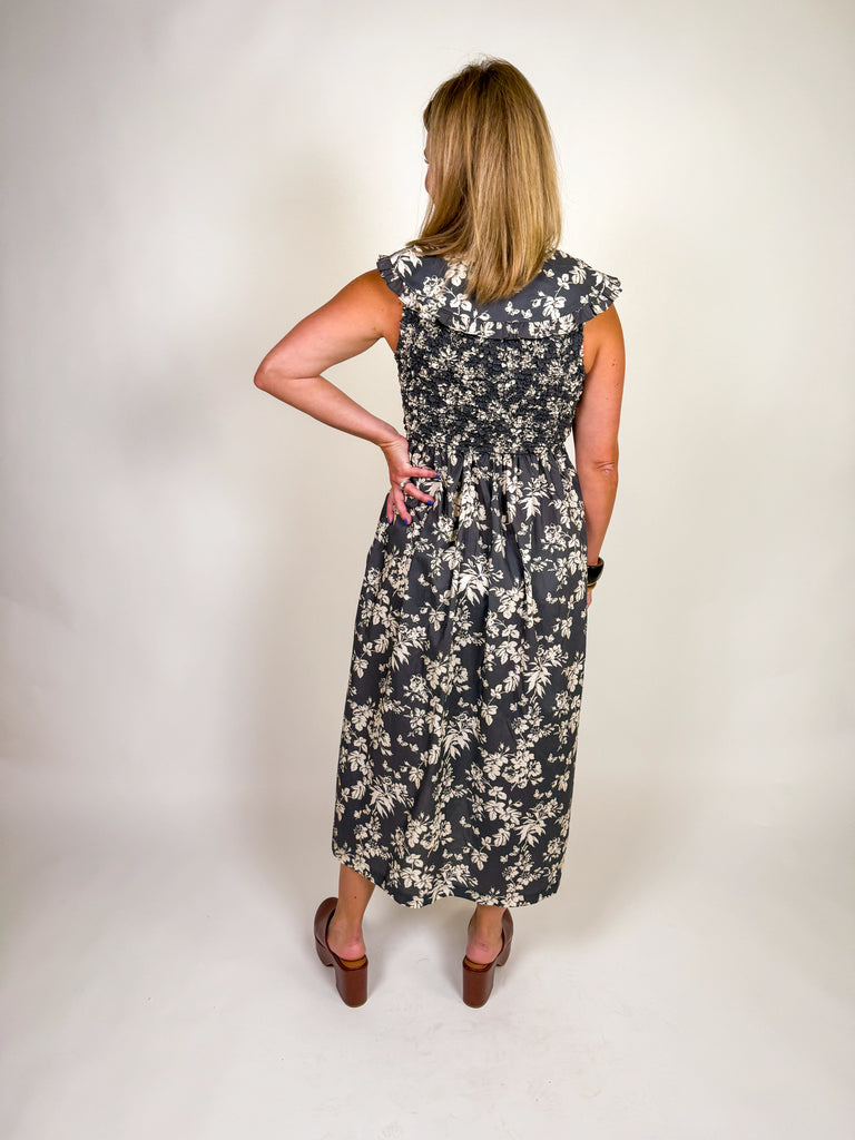 Woman wearing a black floral midi dress with smocked bodice, ruffled sleeves, and tie-front neckline