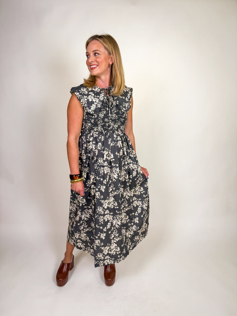 Woman wearing a black floral midi dress with smocked bodice, ruffled sleeves, and tie-front neckline