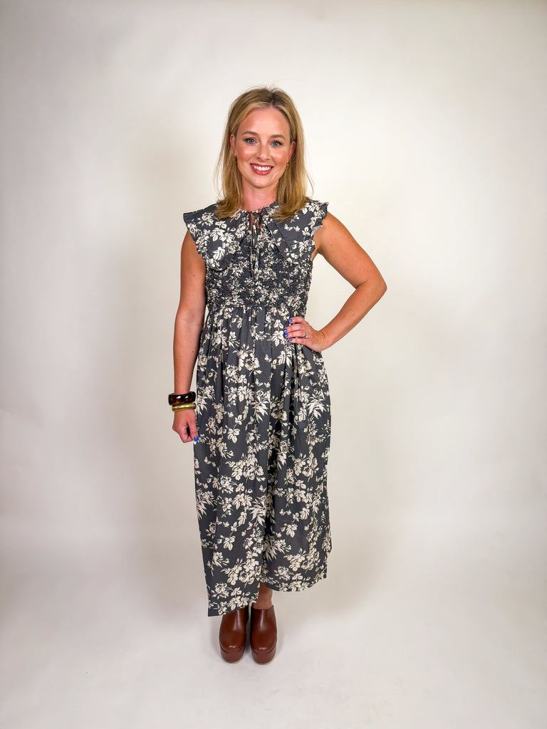 Woman wearing a black floral midi dress with smocked bodice, ruffled sleeves, and tie-front neckline