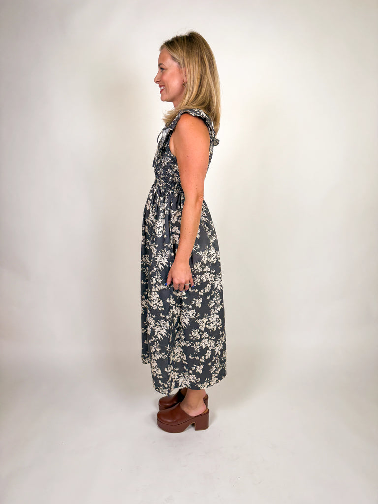 Woman wearing a black floral midi dress with smocked bodice, ruffled sleeves, and tie-front neckline