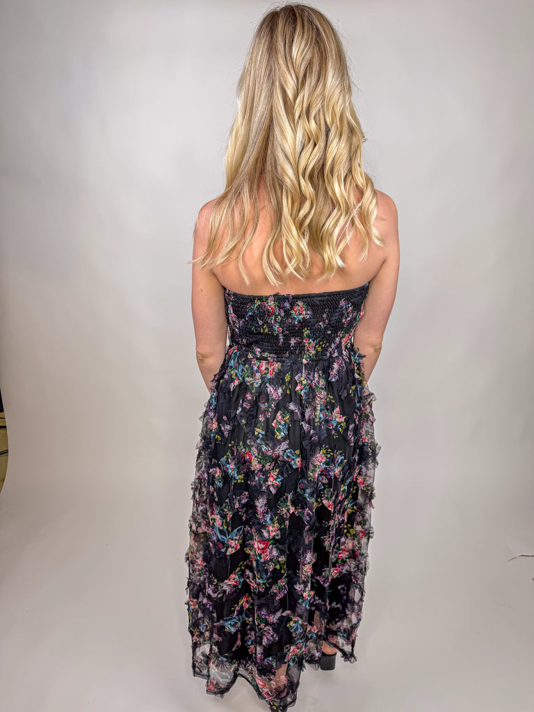 model wearing black strapless floral chiffon midi dress with ruffle details