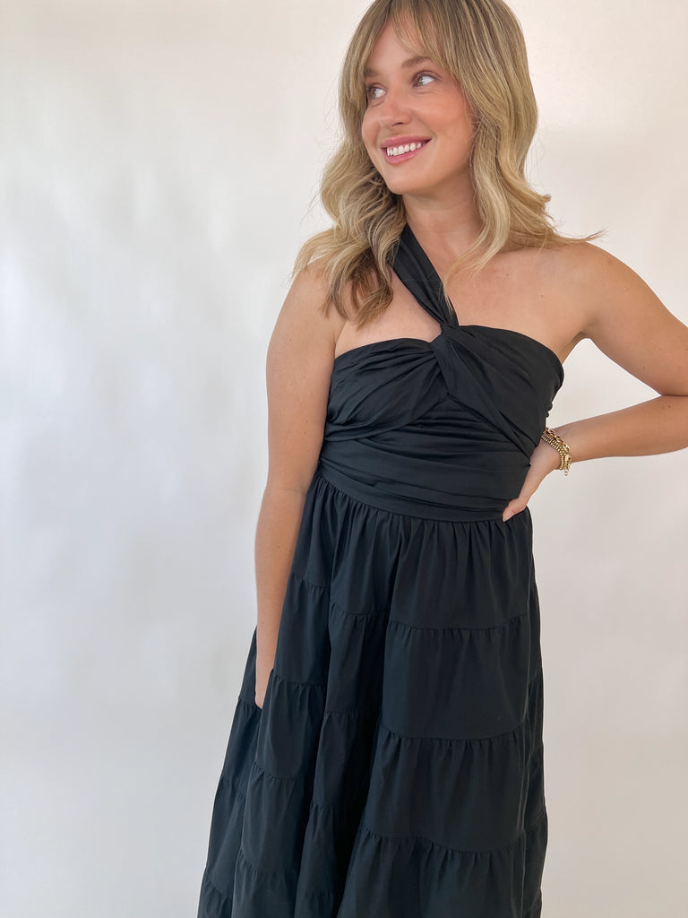 Woman wearing one-shoulder black tiered midi dress with twisted strap detail