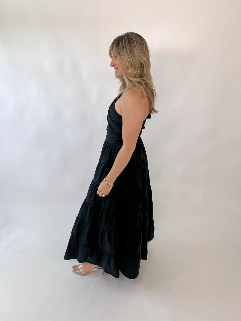 Woman wearing one-shoulder black tiered midi dress with twisted strap detail