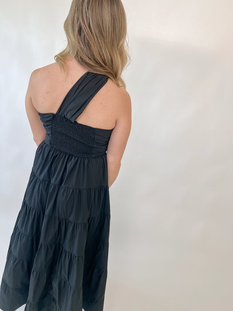 Woman wearing one-shoulder black tiered midi dress with twisted strap detail