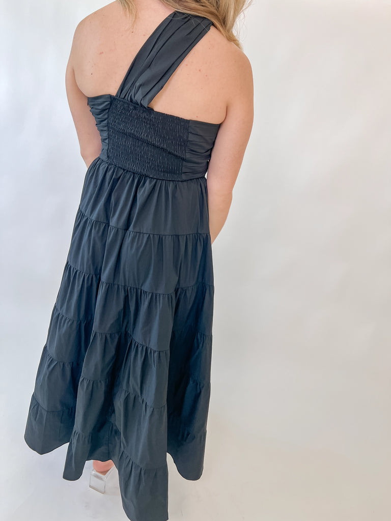 Woman wearing one-shoulder black tiered midi dress with twisted strap detail
