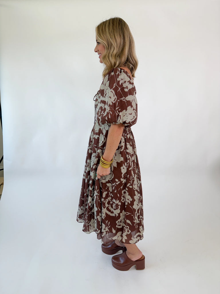 Woman wearing mocha brown puff-sleeve midi dress with cream floral print, square neckline, fitted bodice, and flowy skirt