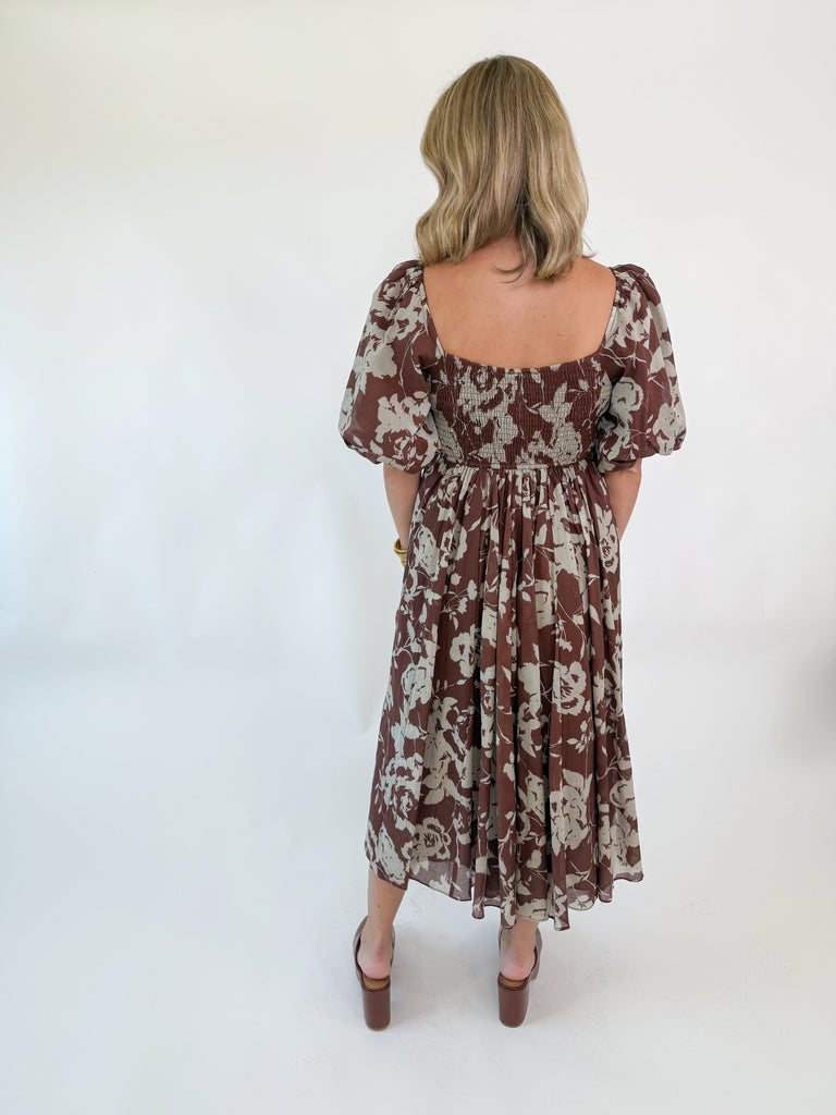 Woman wearing mocha brown puff-sleeve midi dress with cream floral print, square neckline, fitted bodice, and flowy skirt