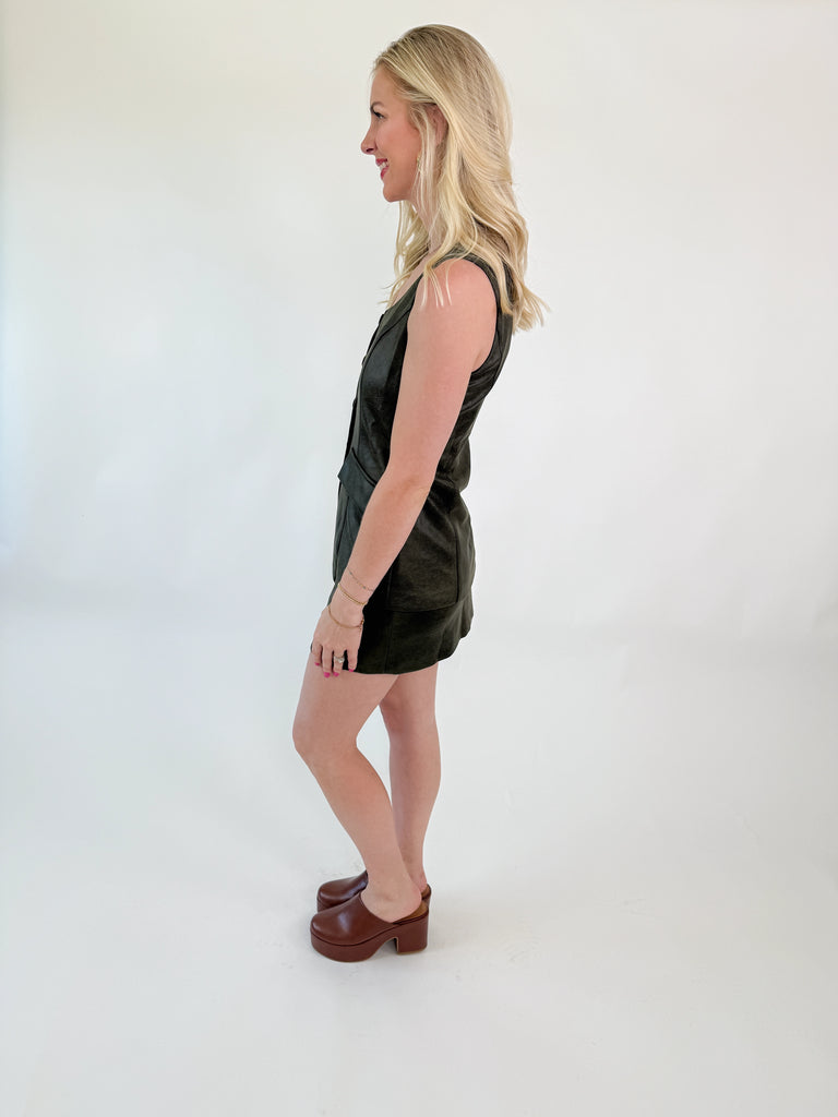 Woman wearing an olive 3-in-1 romper dress with button front and mini skirt overlay