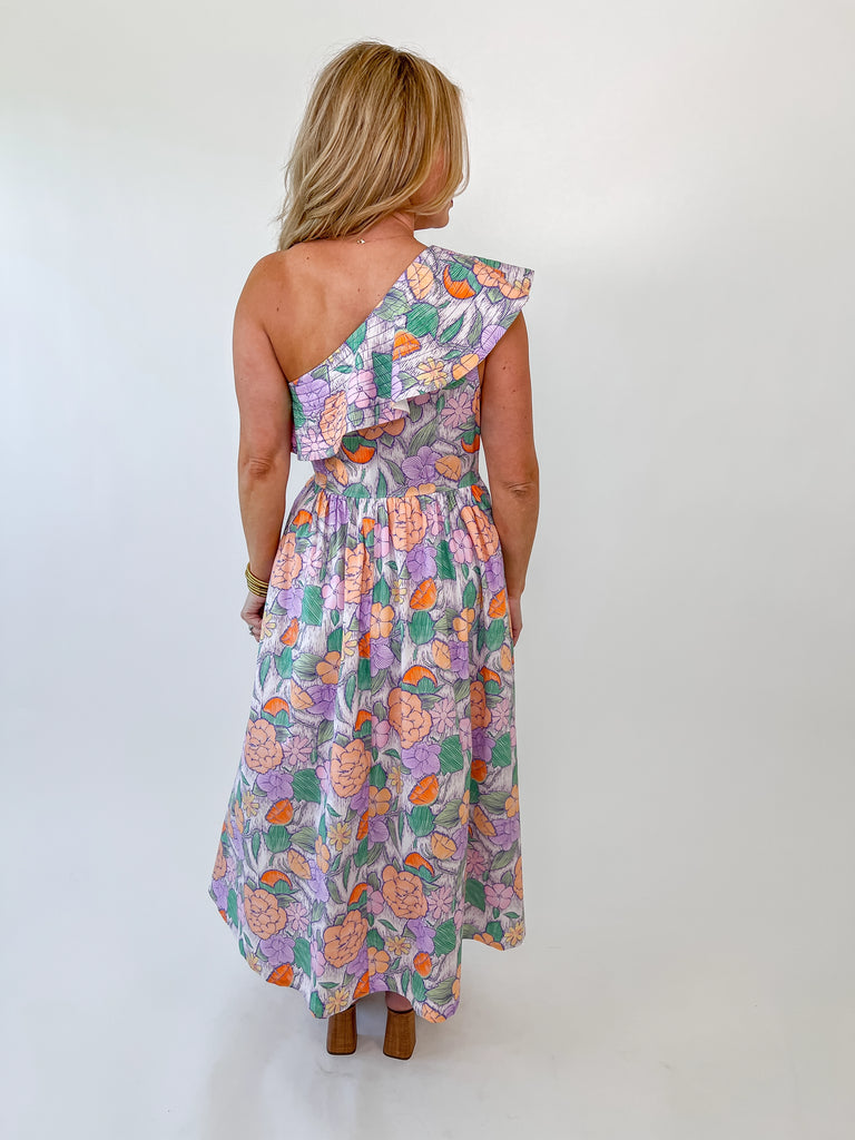 Woman wearing a pastel floral one-shoulder maxi dress with ruffle detail and a smocked waist