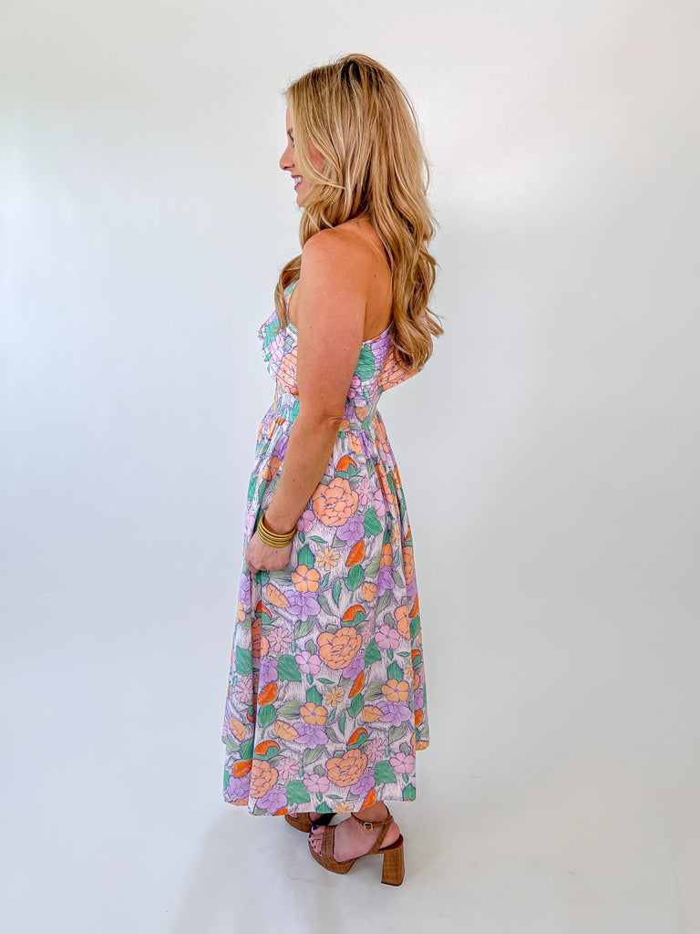 Woman wearing a pastel floral one-shoulder maxi dress with ruffle detail and a smocked waist