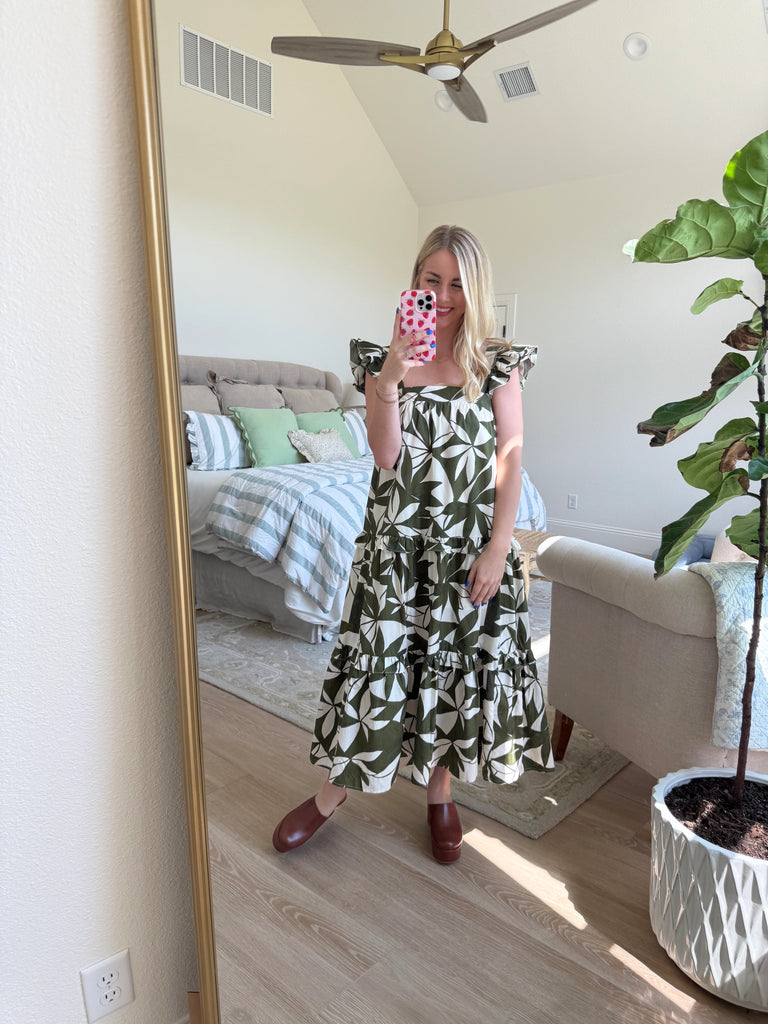 Woman wearing an olive and ivory leaf-print maxi dress with ruffle straps, square neckline, tiered skirt, and open back bow