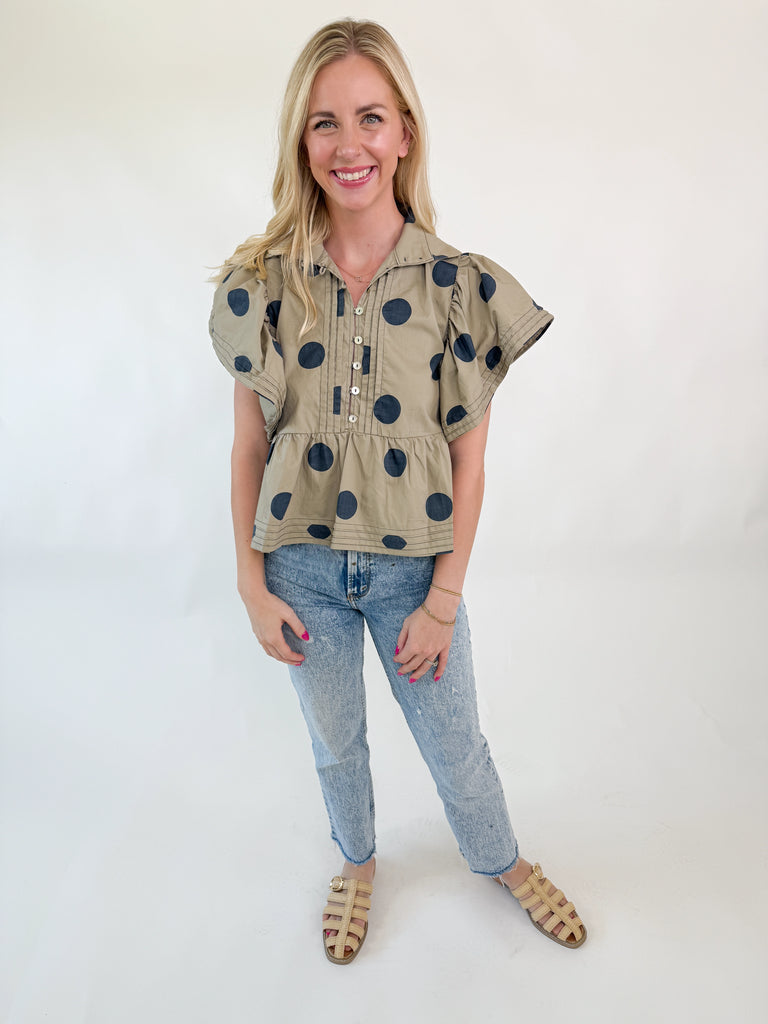 Woman wearing taupe polka dot ruffle sleeve top with button-front and peplum hem