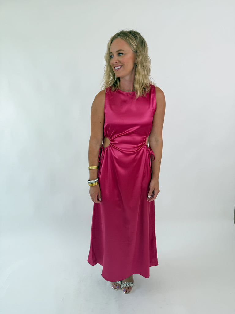 Woman wearing a sleeveless satin hot pink dress with side cutouts and drawstring ties