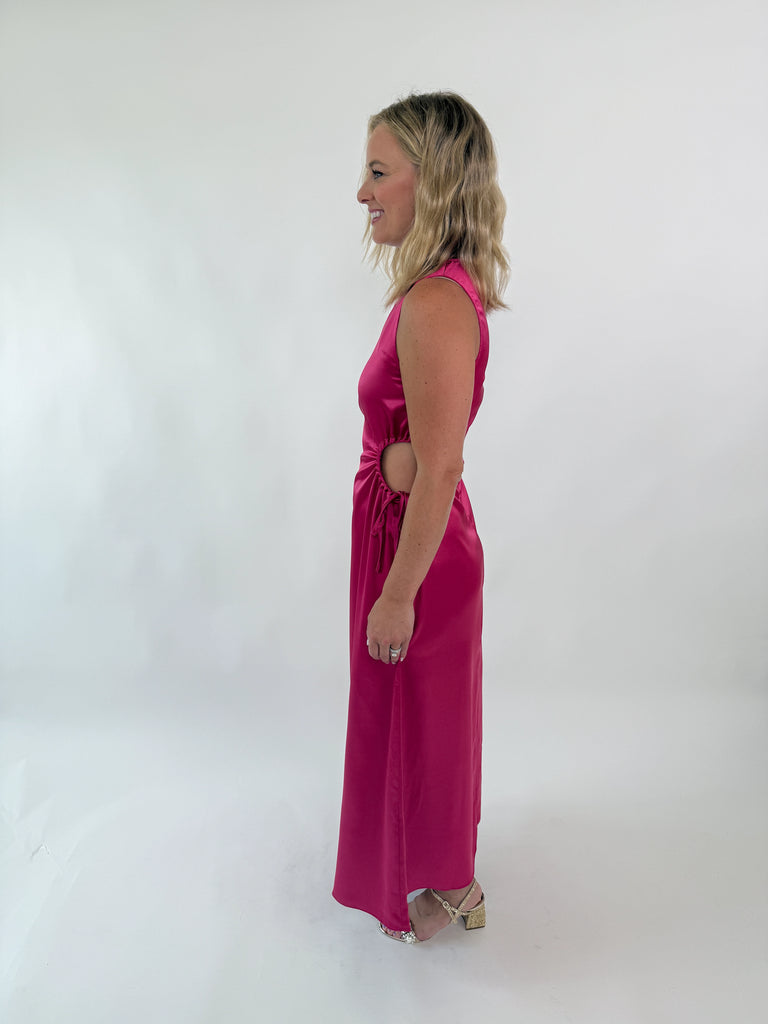 Woman wearing a sleeveless satin hot pink dress with side cutouts and drawstring ties