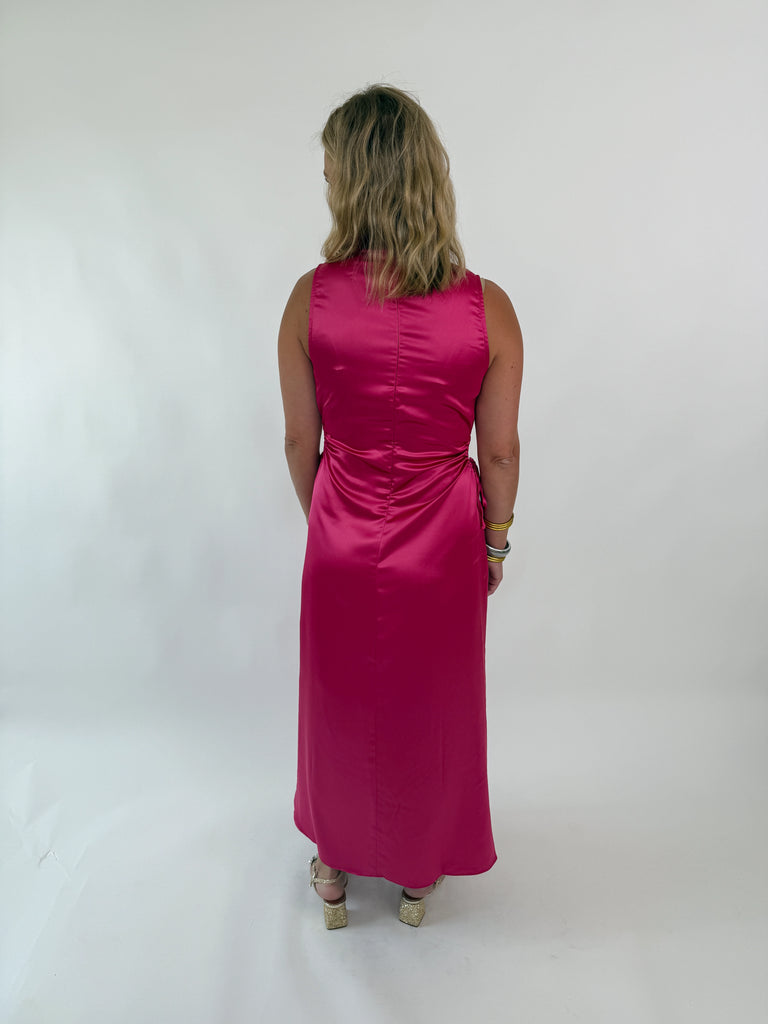 Woman wearing a sleeveless satin hot pink dress with side cutouts and drawstring ties