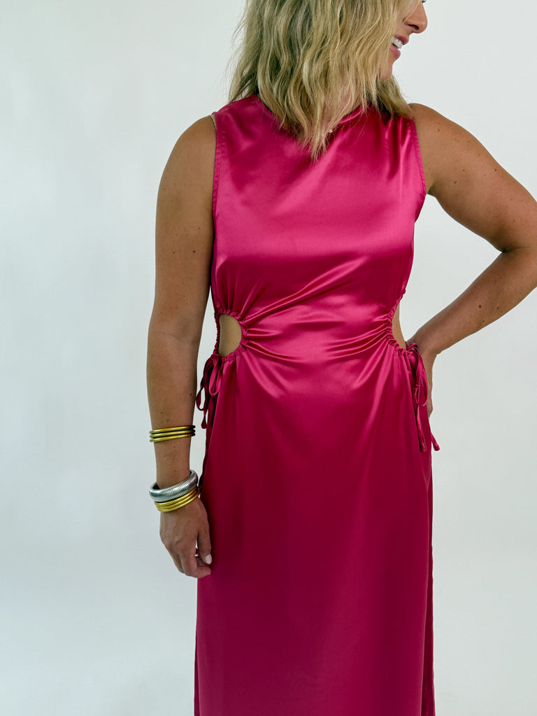 Woman wearing a sleeveless satin hot pink dress with side cutouts and drawstring ties