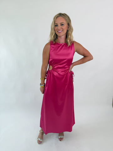 Woman wearing a sleeveless satin hot pink dress with side cutouts and drawstring ties