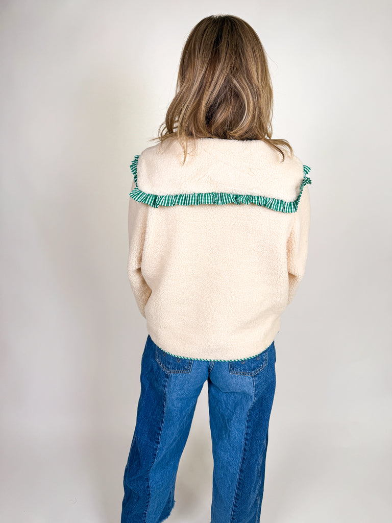 Woman wearing a cozy sherpa jacket with oversized ruffle-trimmed collar, contrast striped detail, and button front closure in blue, green, and latte.