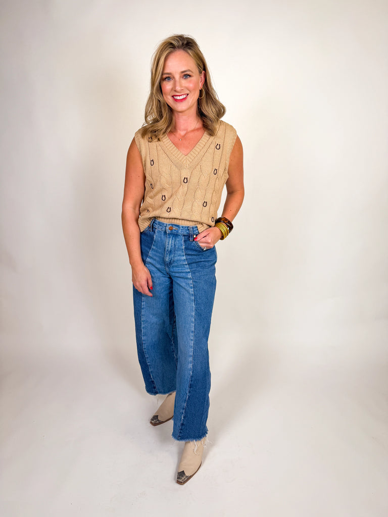 Woman wearing a camel cable knit vest with embroidered horseshoes and a deep V-neckline
