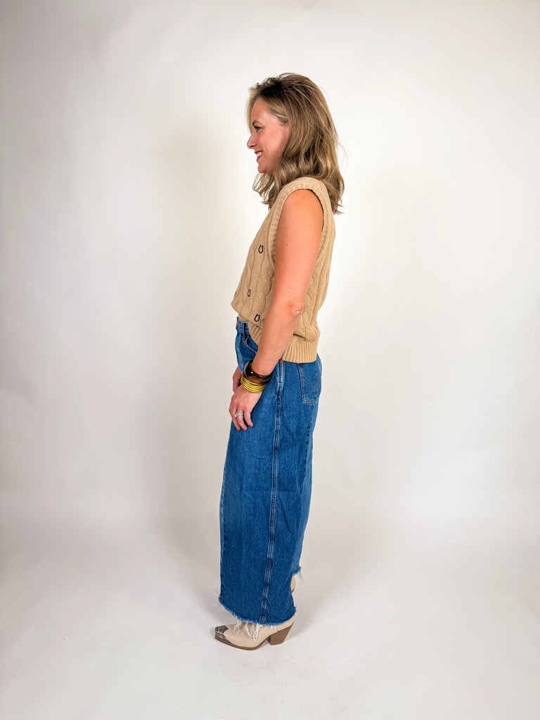 Woman wearing a camel cable knit vest with embroidered horseshoes and a deep V-neckline