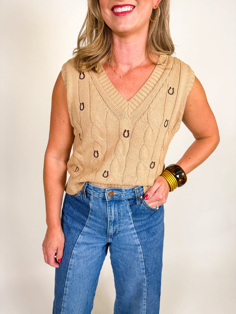 Woman wearing a camel cable knit vest with embroidered horseshoes and a deep V-neckline