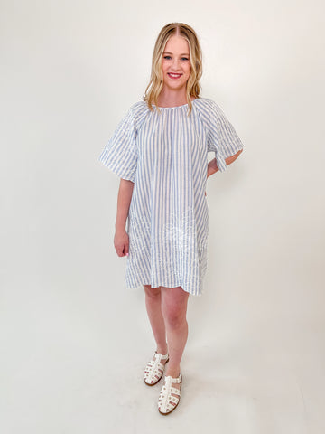 Woman wearing a blue and white striped dress with flutter sleeves, floral embroidery, and a back bow detail