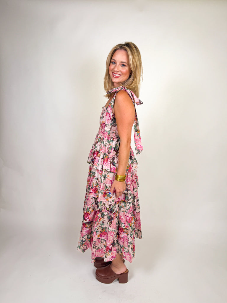 Woman wearing a tiered pink floral smocked maxi dress with tie straps and ruffle details