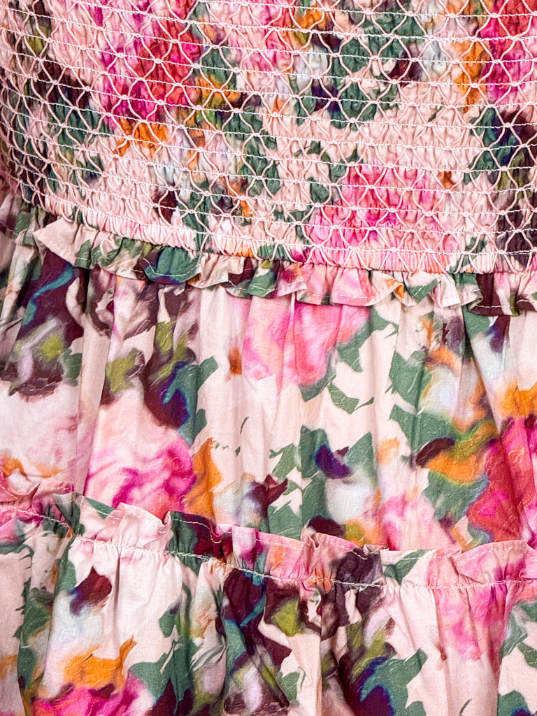 Woman wearing a tiered pink floral smocked maxi dress with tie straps and ruffle details