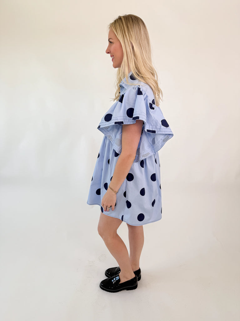 Light blue mini dress with navy polka dots, collared neckline, button-down front, and flutter sleeves.