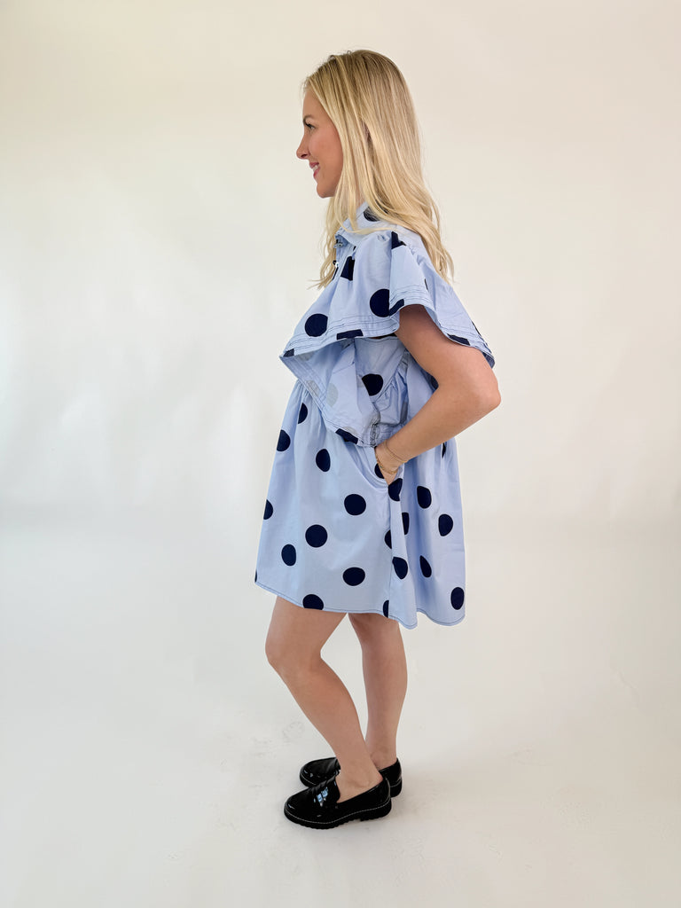 Light blue mini dress with navy polka dots, collared neckline, button-down front, and flutter sleeves.